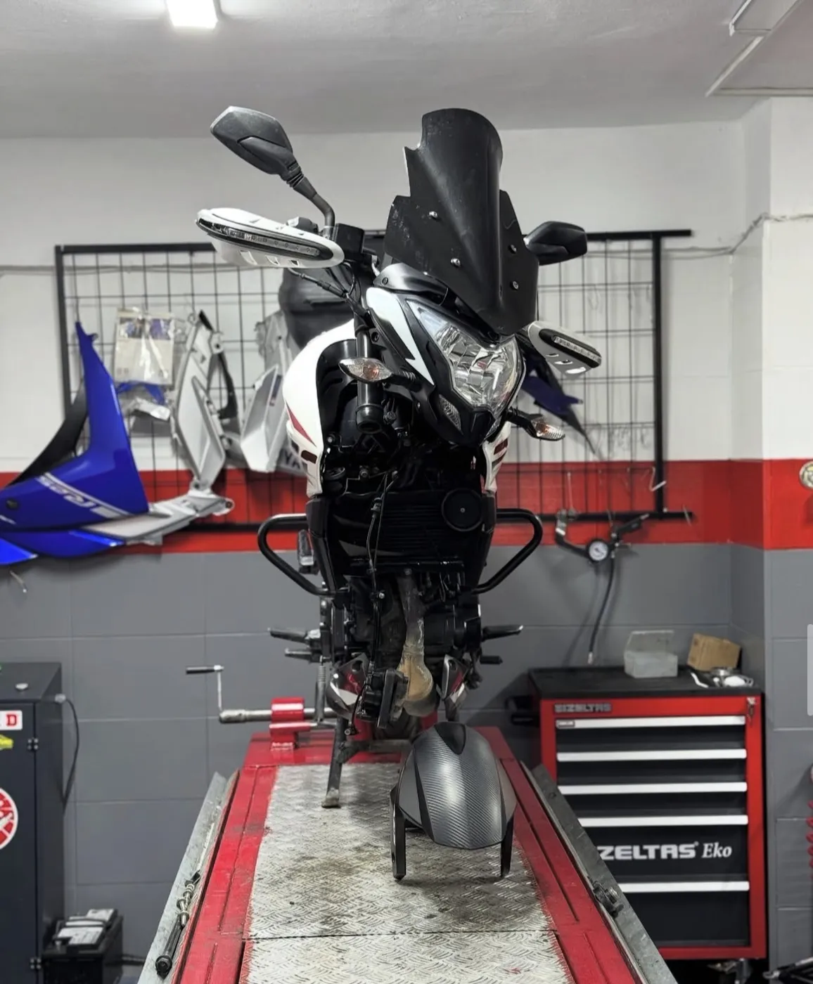 Lift üzerindeki motosiklet ve duvarda bekleyen grenaj parçaları